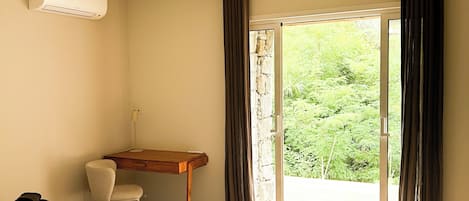 A hotel room with a bed, a desk, a chair, and a view of greenery through the window.