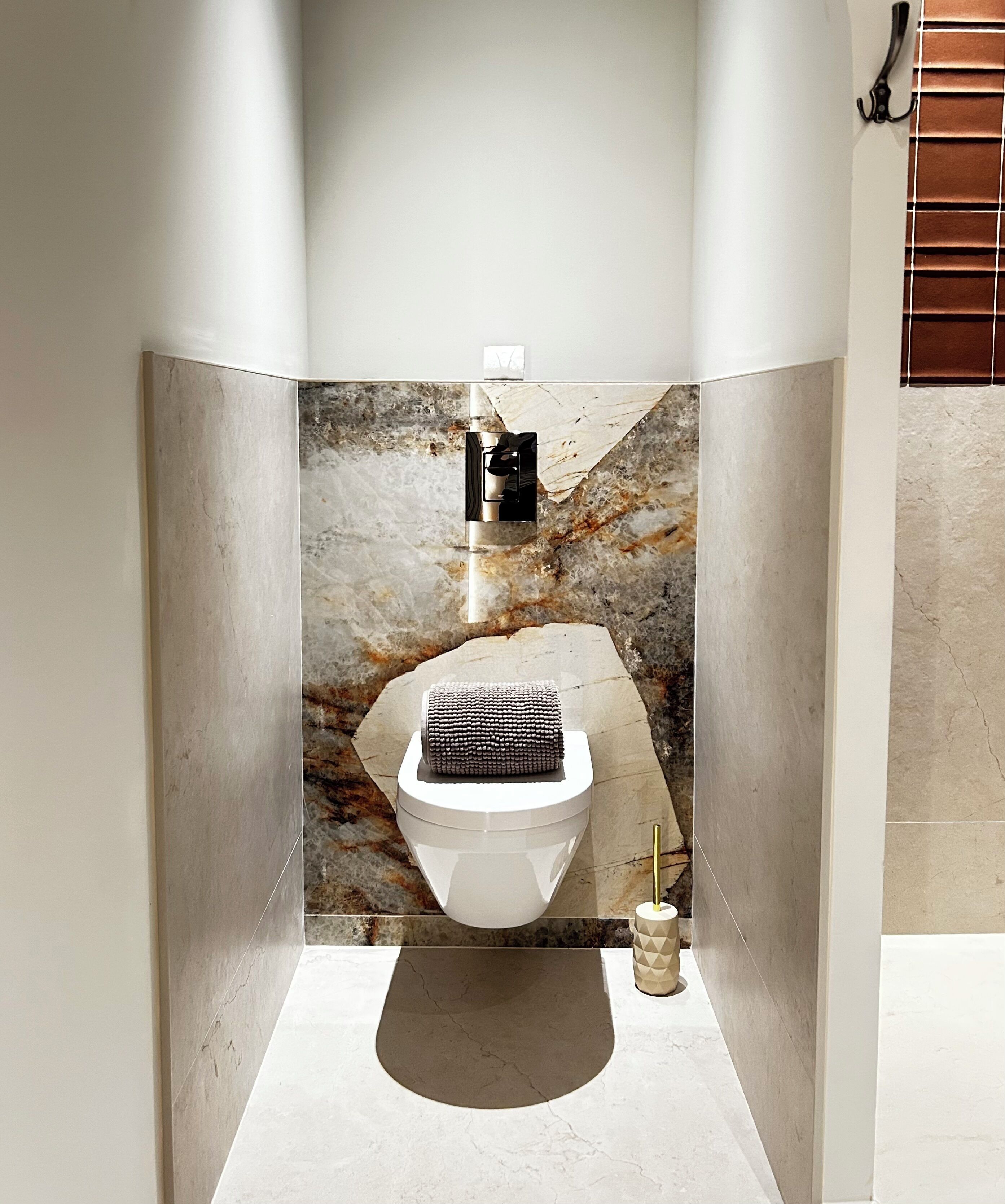 A bathroom with a marble wall, a toilet, a towel, and a toilet paper holder.