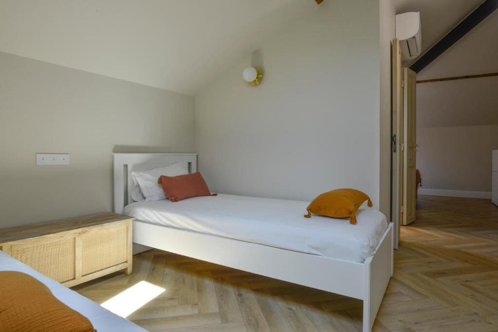 Habitación con una cama individual, suelo de madera, cama blanca, mesita de noche y lámpara de pared.