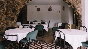 A restaurant with stone arches, round tables with white tablecloths, and green chairs. - L'Orangeraie d'Afa (Afa)