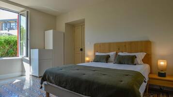 Quarto com cama, luminárias de cabeceira, guarda-roupa e porta que dá para uma varanda.