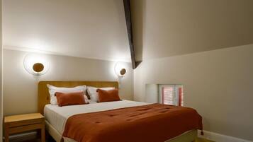 A bedroom with a bed, nightstand, wall-mounted lights, and a window with blinds.