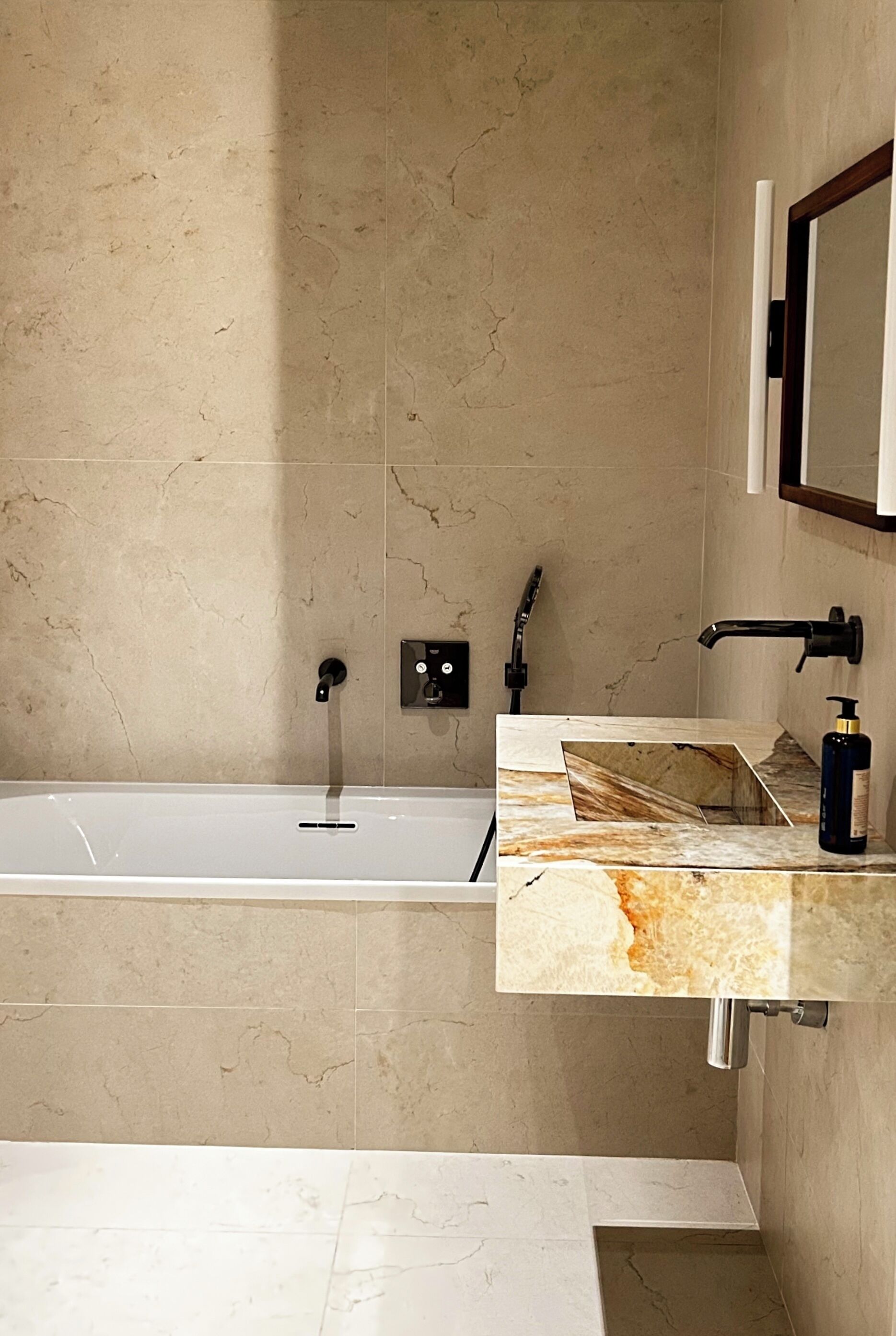 A modern bathroom with a bathtub, a vanity with a marble countertop, and a wall-mounted mirror.