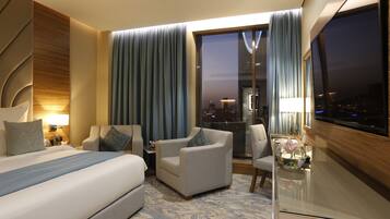 Una habitación de hotel moderna con una cama grande, dos sillones, una mesita y un televisor.