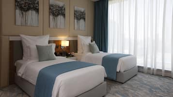 A hotel room with two beds, a nightstand, and a large window with sheer curtains.
