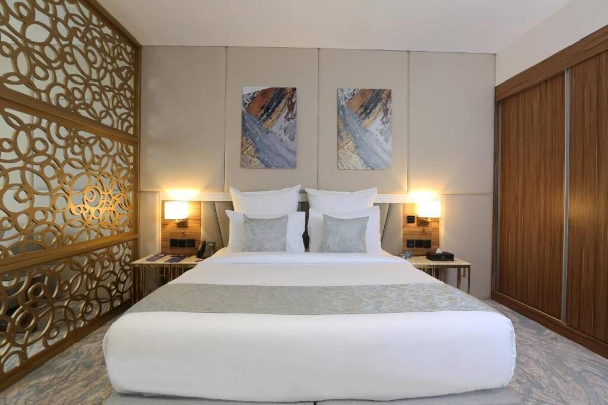 A large bed with white linens, two wall-mounted lamps, and abstract artwork above it.