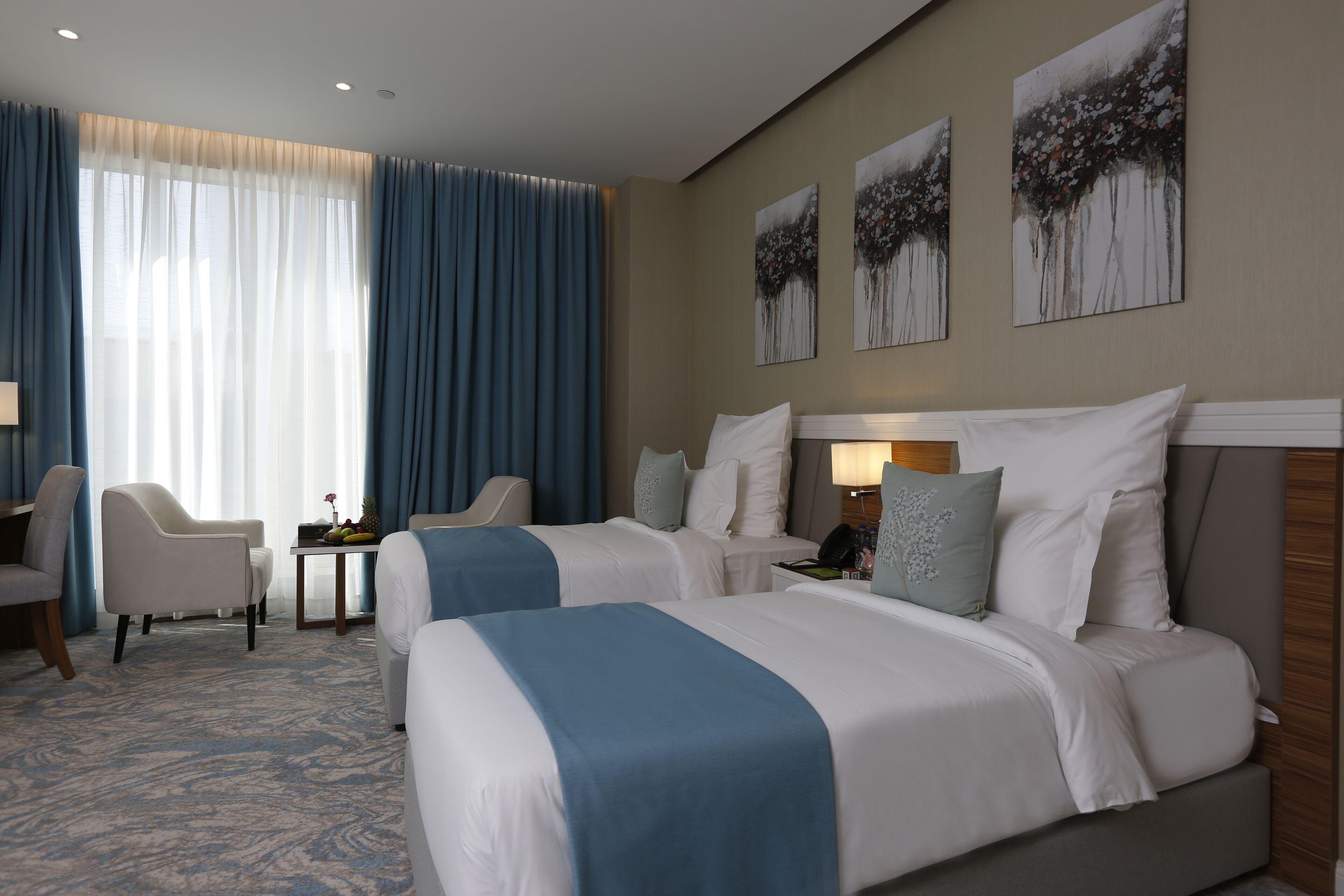 A hotel room with two beds, a desk, a chair, and artwork on the wall.
