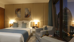 Een hotelkamer met twee bedden, een sofa, een kleine tafel met fruit, en uitzicht op de stad.