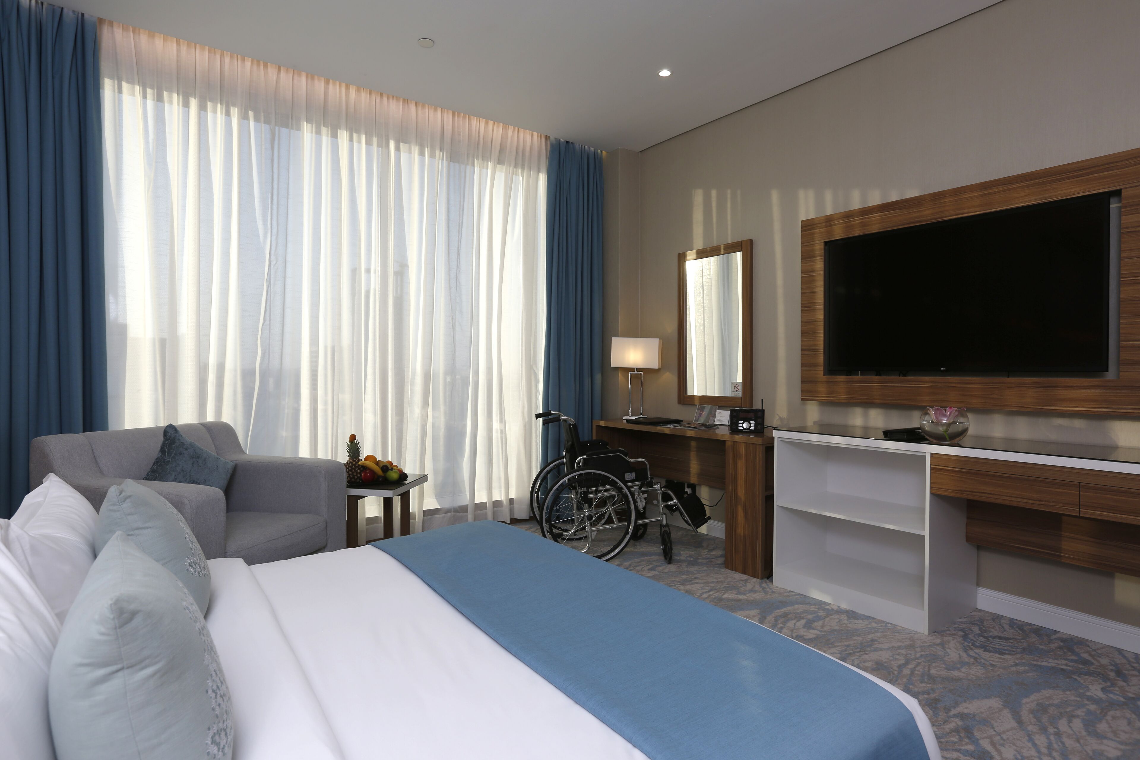 Una habitación de hotel con una cama, un escritorio, una silla de ruedas y un televisor en la pared.