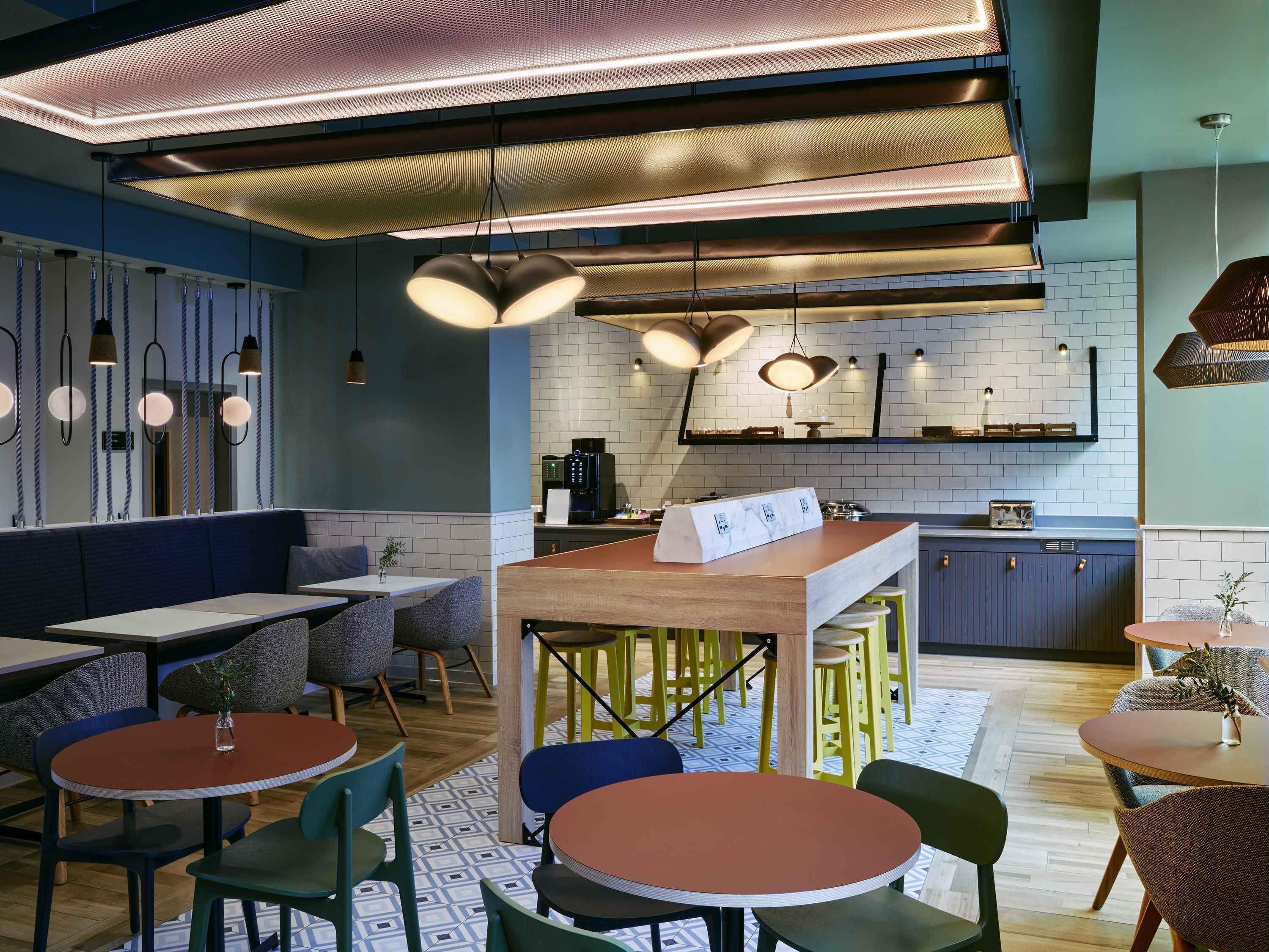 A modern restaurant interior with high ceilings, pendant lighting, and a mix of seating arrangements including booths and tables.