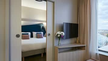 A hotel room with a bed, a TV, a vase with flowers, and a view of a bridge.