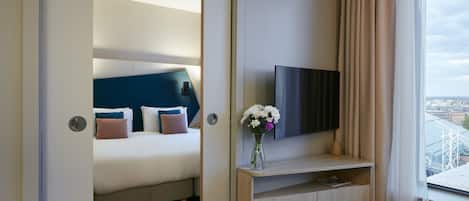 A hotel room with a bed, a TV, a vase with flowers, and a view of a bridge.