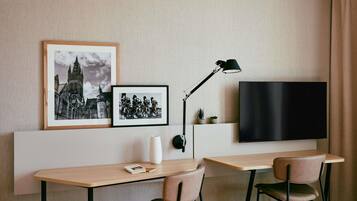 Una habitación de hotel moderna con un televisor de pantalla plana montado en la pared, un escritorio con dos sillas y dos cuadros enmarcados sobre el escritorio.