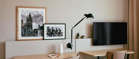 Ein modernes Hotelzimmer mit Flachbildfernseher an der Wand, einem Schreibtisch mit zwei Stühlen und zwei gerahmten Bildern darüber.