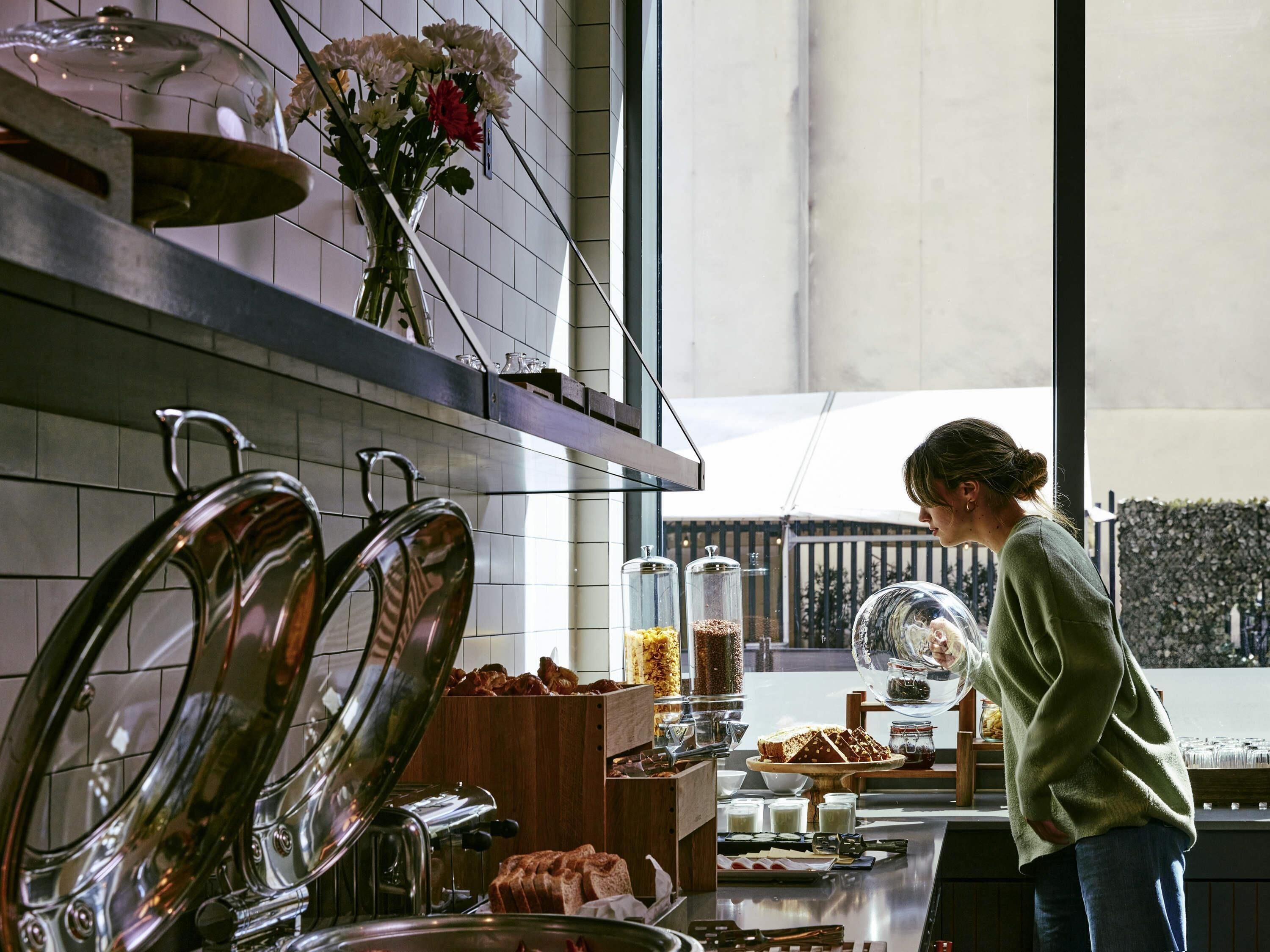 Uma área de cozinha com uma vitrine de pão, uma máquina de café e uma pessoa ao lado do balcão.