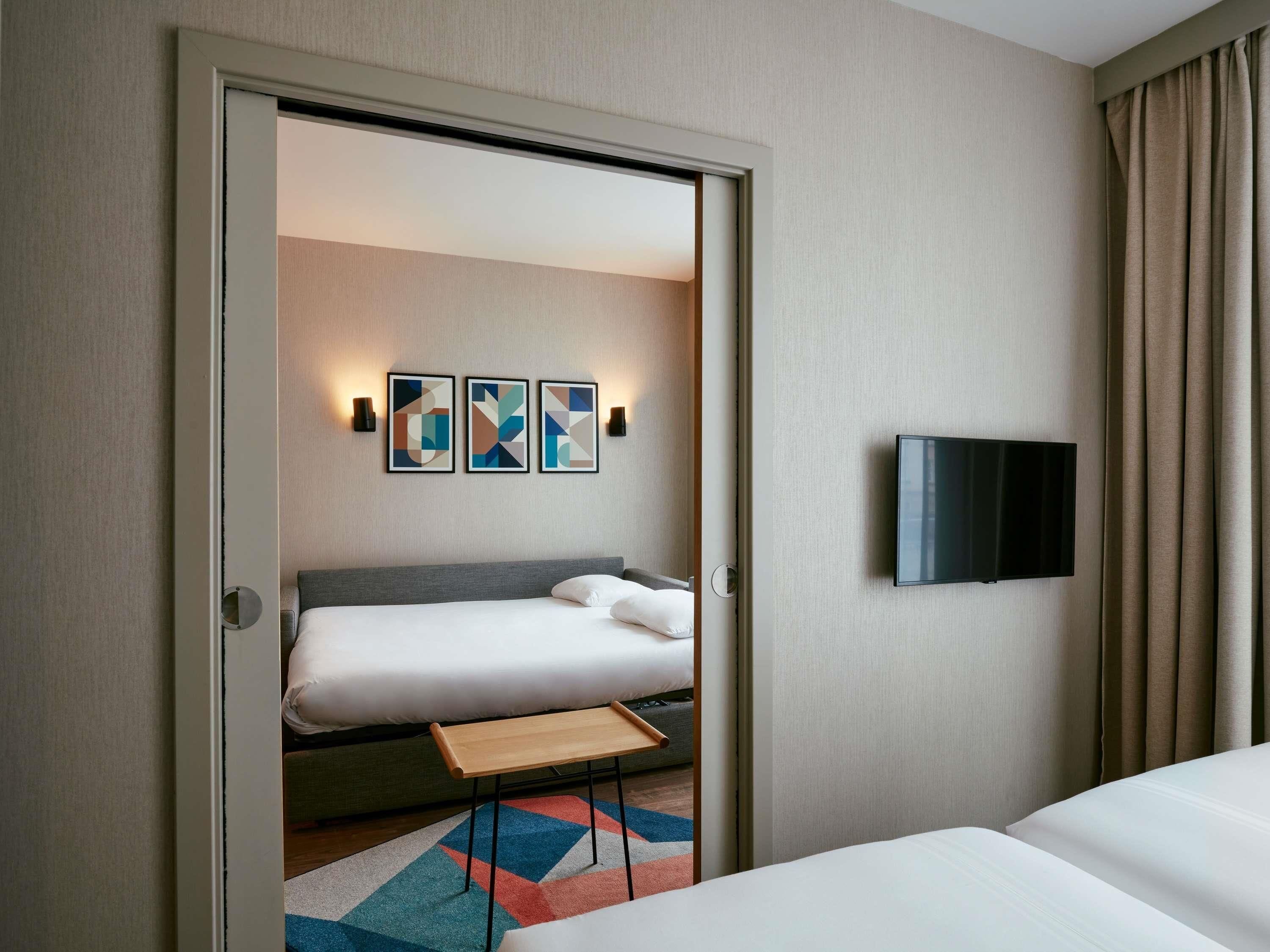 A hotel room with a bed, a TV mounted on the wall, and abstract art on the wall.