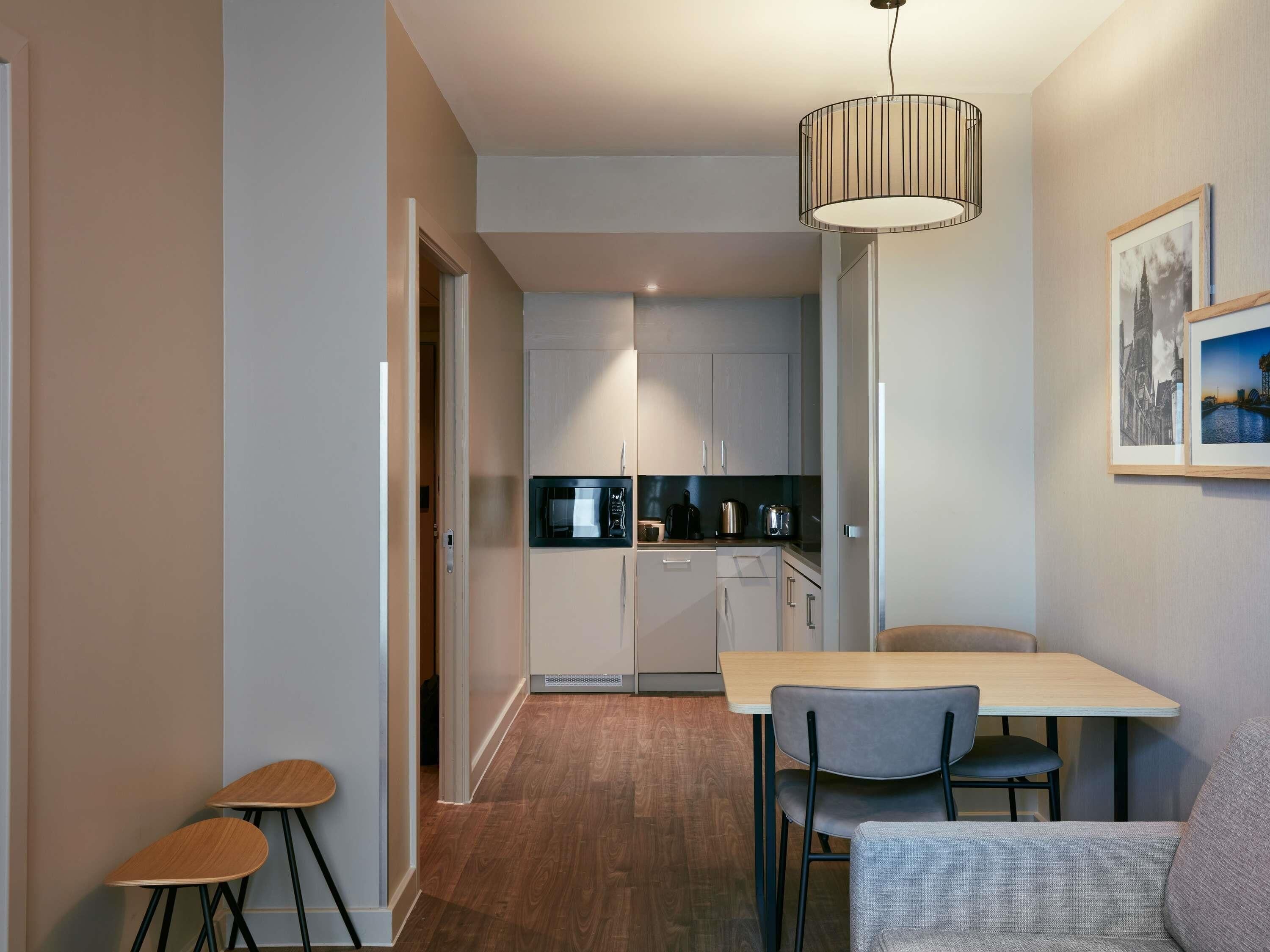 A modern kitchen with a microwave, kettle, and coffee maker, a dining area with a table and chairs, and a hanging light fixture.