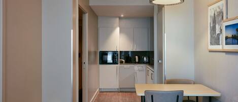 A modern kitchen with a microwave, kettle, and coffee maker, a dining area with a table and chairs, and a hanging light fixture.