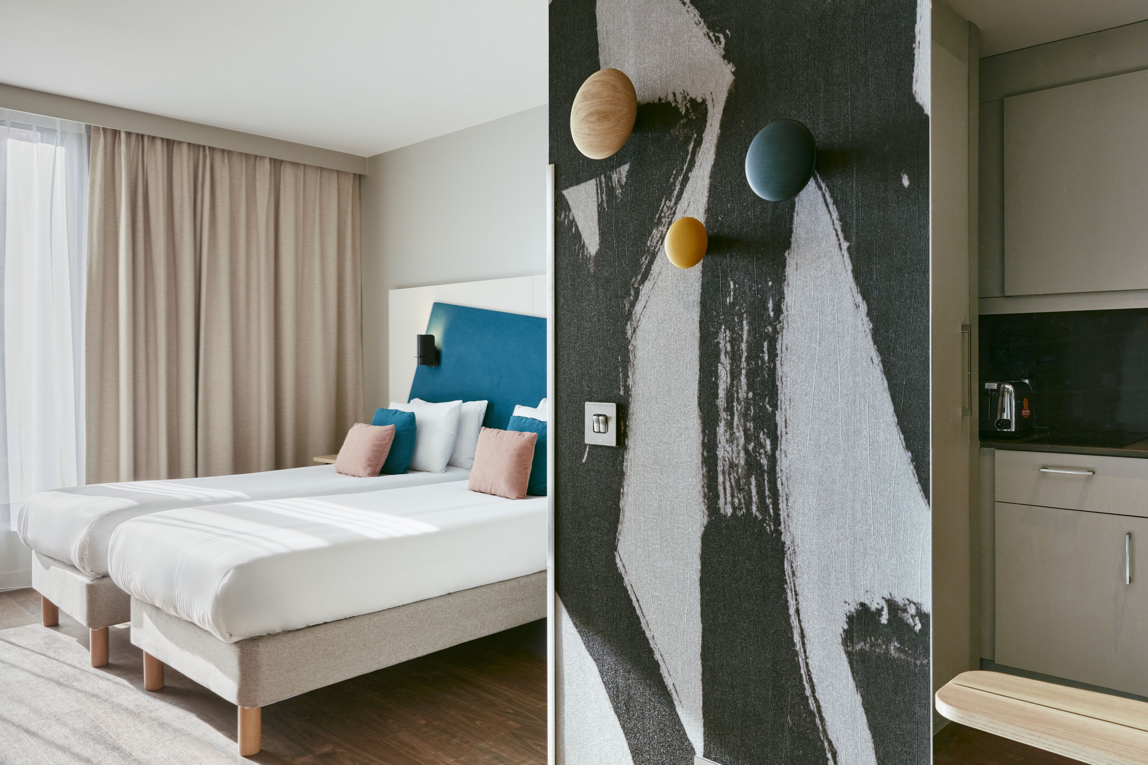 Ein modernes Hotelzimmer mit einem großen Bett, einer blauen Akzentwand und einer Küchenzeile mit Schränken und einer Arbeitsplatte.