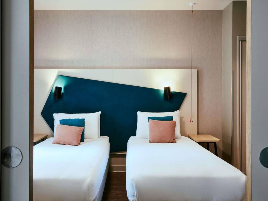 Een hotelkamer met twee bedden, een groot turquoise hoofdeinde en bedlampjes.