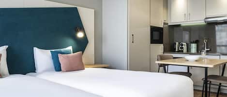 A hotel room with a bed, a desk, and a kitchenette.