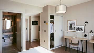 Una habitación de hotel moderna con cama, escritorio con silla, armario, baño con lavamanos y espejo.