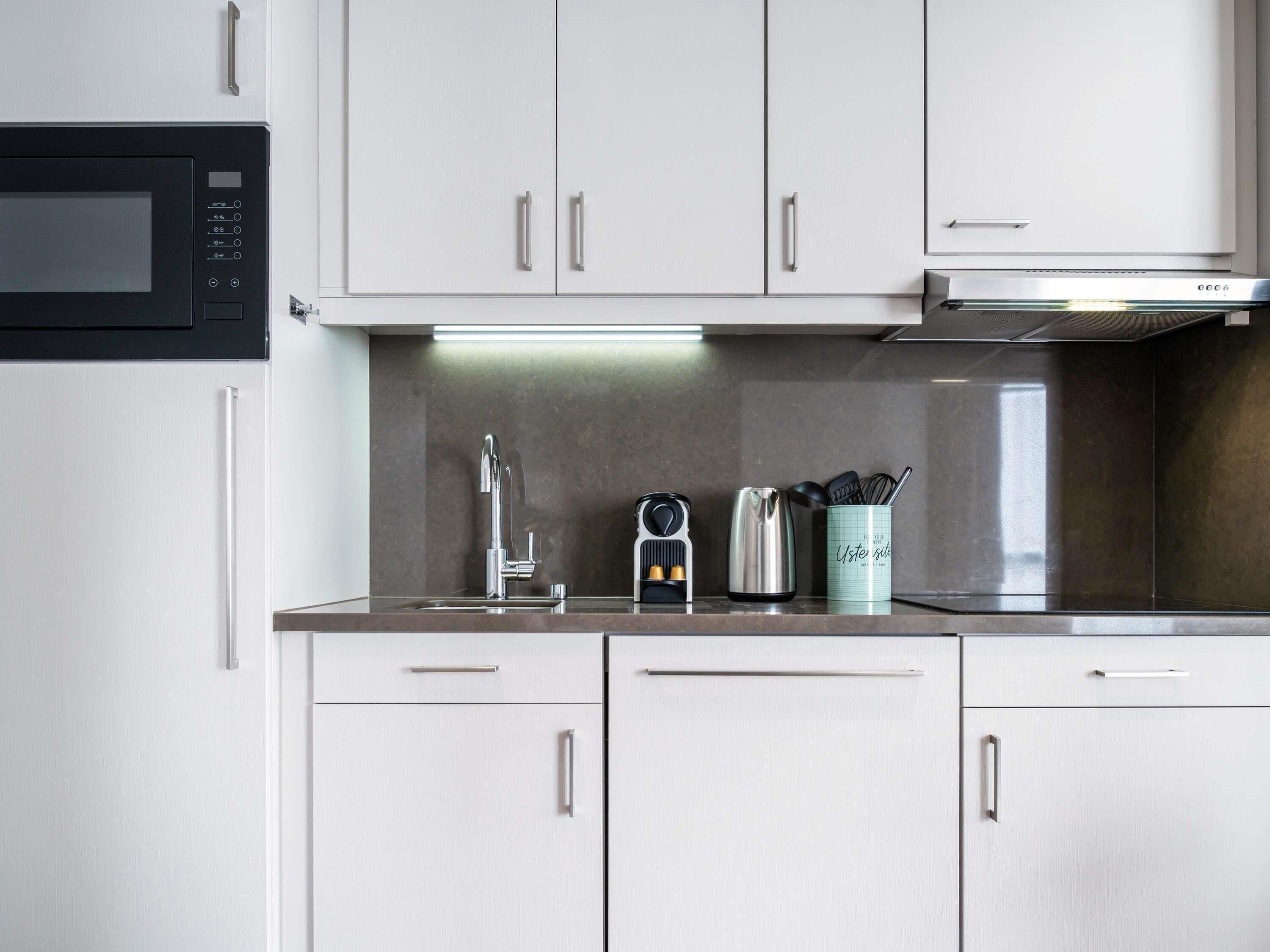 A modern kitchen with white cabinets, a stainless steel sink, a kettle, and a coffee maker.