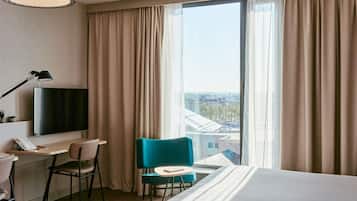 A hotel room with a bed, a desk, a chair, a TV, and a window with curtains.