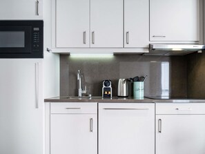A modern kitchen with white cabinets, a stainless steel sink, a kettle, and a coffee maker.