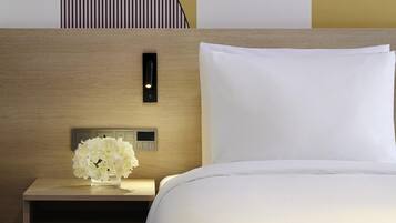 A neatly made bed with white linens, a bedside table with a vase of white flowers, and a wall-mounted control panel.
