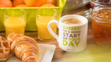 Une table dressée pour le petit-déjeuner avec des croissants, du jus d’orange et une tasse ornée d’un message.