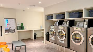 A laundry facility with multiple washing machines, a small table, and a trash bin.