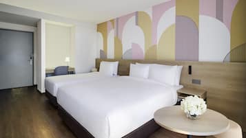 Une chambre d’hôtel avec un grand lit, une table de chevet ornée d’un vase de fleurs et un mur décoré d’œuvres d’art abstraites.