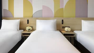 A hotel room with three beds, a wooden headboard, bedside tables with lamps, and a decorative wall.