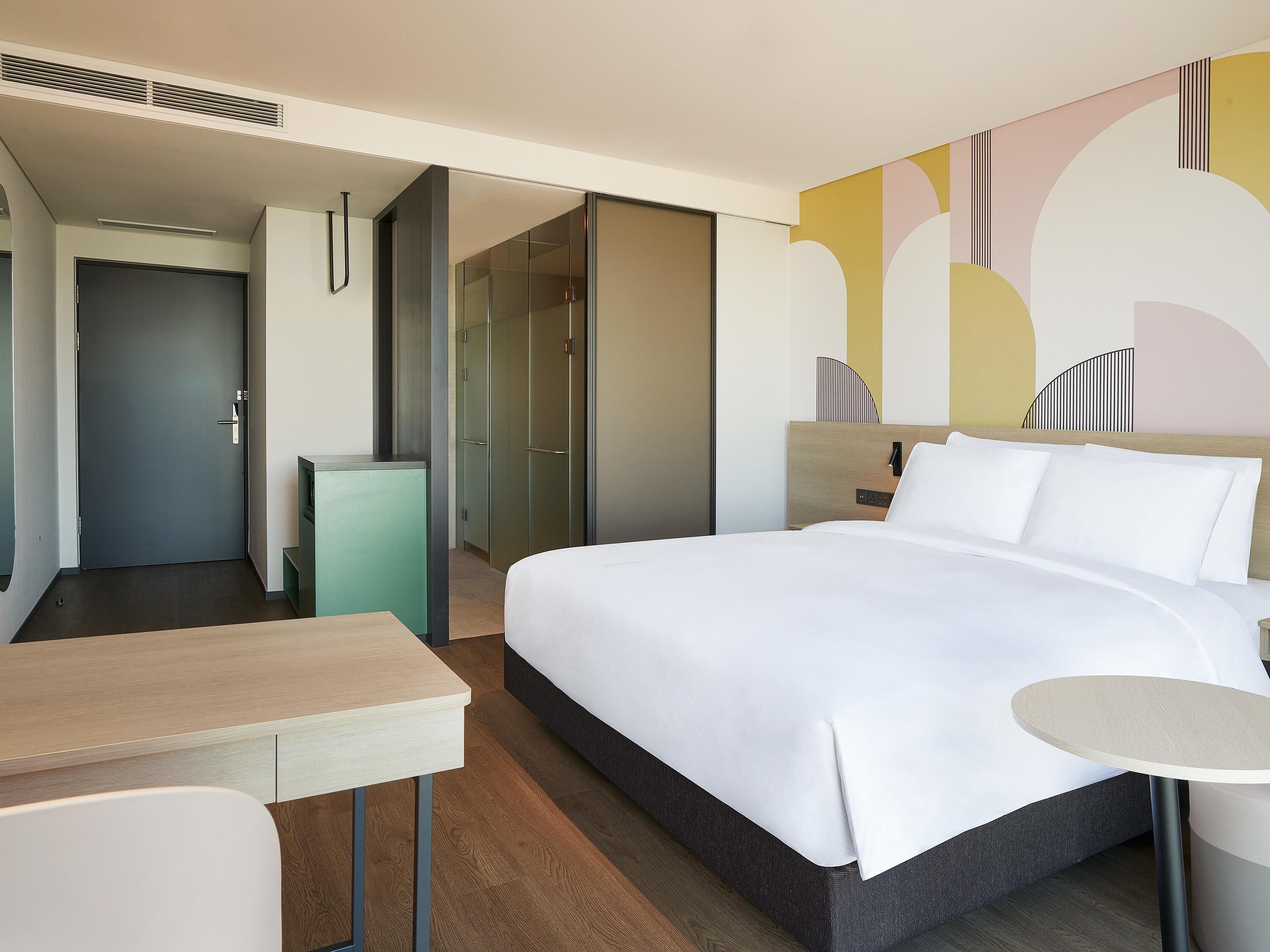 Une chambre d’hôtel moderne, équipée d’un lit, d’une table de chevet et d’un petit bureau.