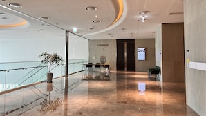 Un hall d’entrée moderne avec une rambarde en verre, un espace détente avec des tables et des chaises, un escalier et une enseigne indiquant « CHAMPAGNE ».