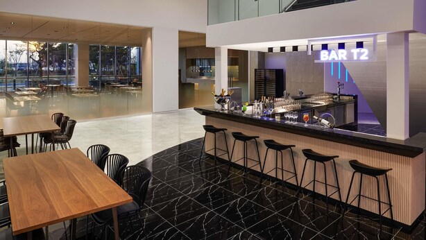 Un espace bar moderne avec une enseigne indiquant « BAR T2 », une rambarde en verre et un escalier.