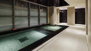 Un espace piscine intérieure moderne, doté de murs en verre et d’une zone de douche séparée.