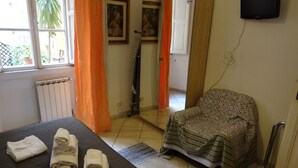 Una habitación de hotel con cama, una silla, un radiador, televisión y ventana con cortinas.