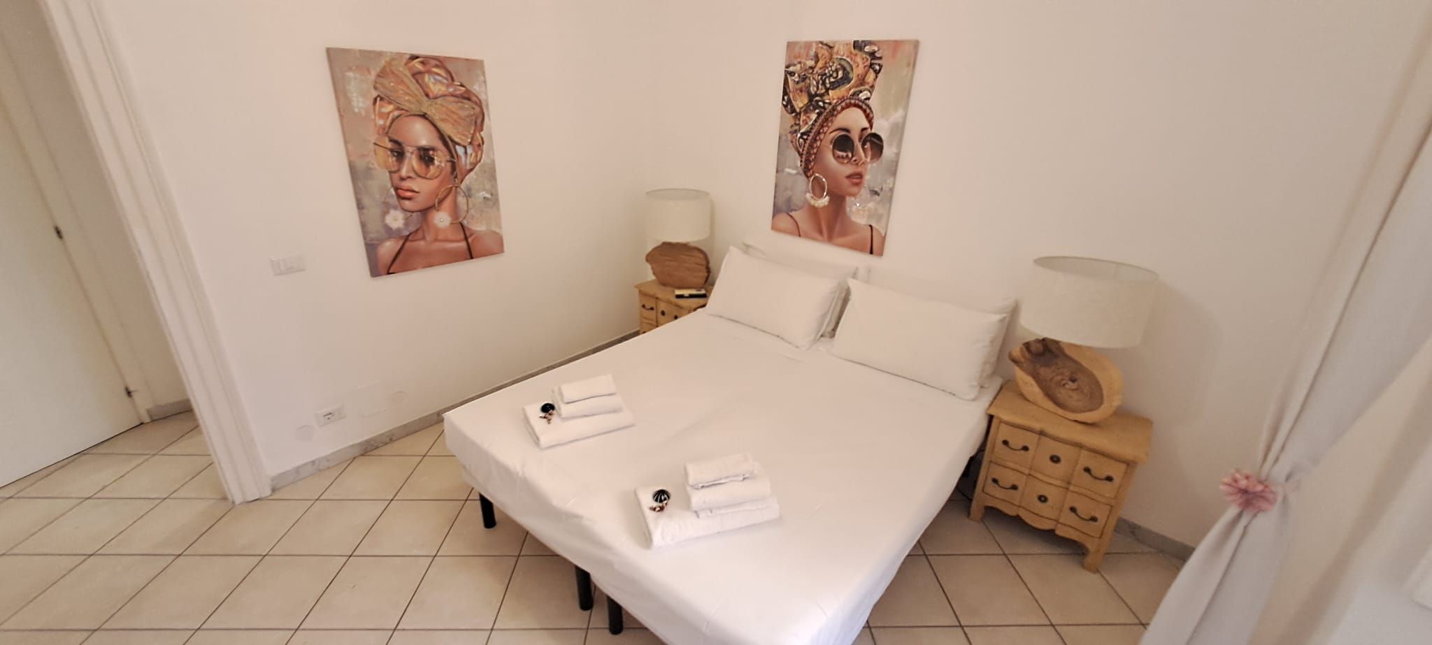 A hotel room with a bed, two nightstands, and two wall-mounted paintings.