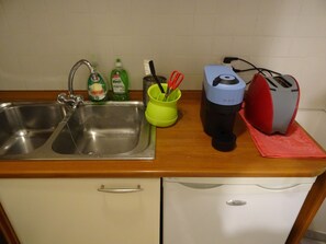 A kitchen with a stainless steel sink, green dish soap, a toothbrush, and a red toaster on the counter.