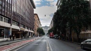 Una calle con edificios, un camión de reparto rojo y un coche aparcado al borde.