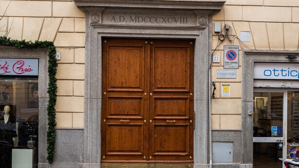 Una gran puerta doble de madera con manijas de bronce, un cartel encima que dice "A.D. MDCCCXCVII" y un letrero de "condominio" a la derecha.