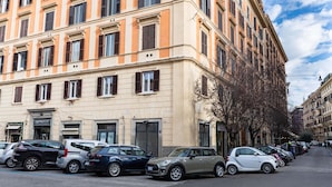 Fila de coches estacionados a lo largo de una calle, con un edificio que tiene varias ventanas y una puerta.