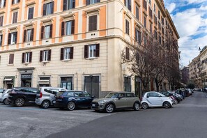 A row of parked cars along a street with a building featuring multiple windows and a door.