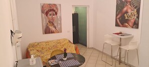A living room with a sofa, a small round table, and a chair. There are two paintings on the wall. - Apartment (Roma)