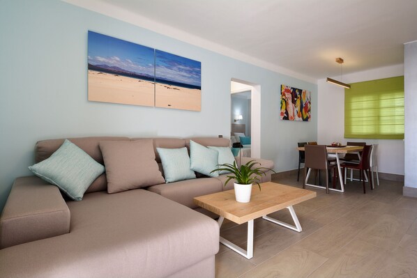 Un salon avec un canapé beige, une table basse en bois et un coin repas comprenant une table et des chaises.