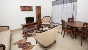 A living room with a sofa, a TV, a wooden cabinet, a dining table with chairs, and a patterned rug.