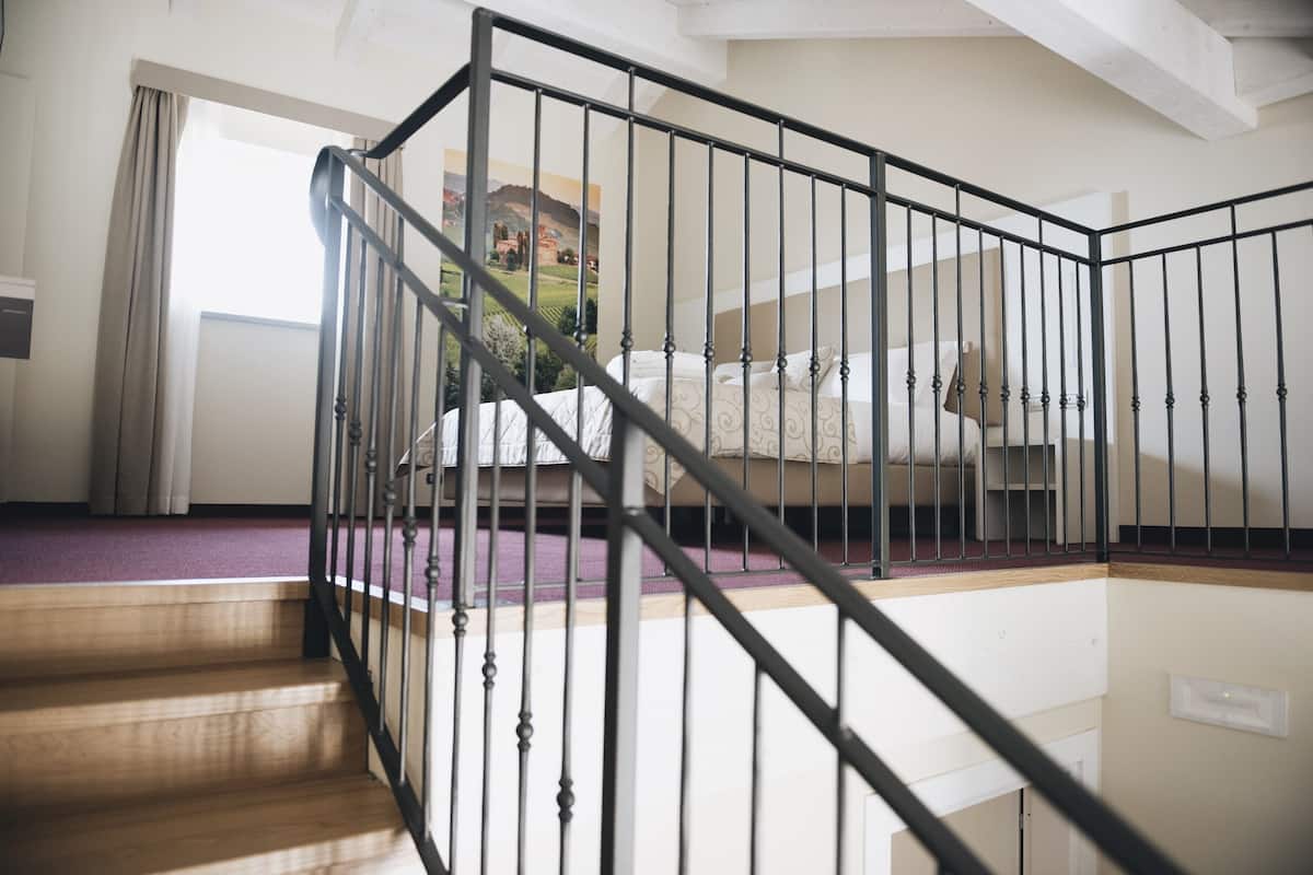 A staircase with a black railing leading to a bedroom with a bed and a view of a landscape through a window.