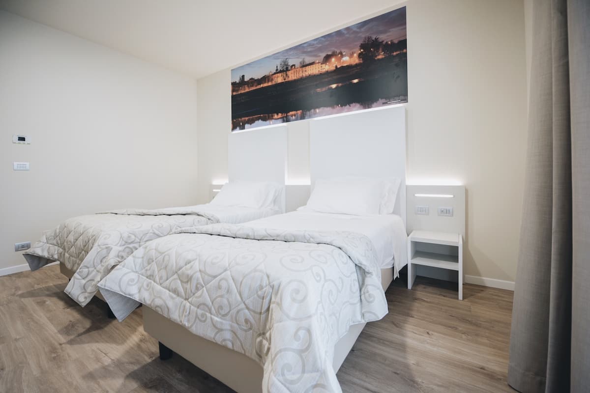 A bedroom with two beds, a nightstand, and a wall-mounted painting.
